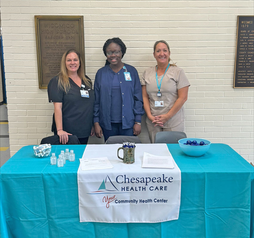 three women standing behind a table with a sign on it