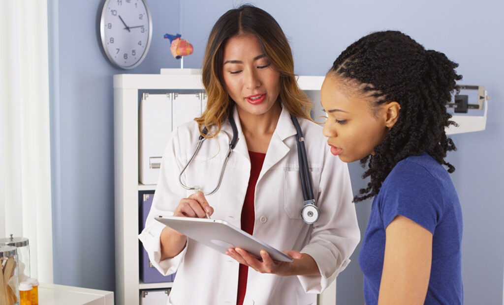 a woman in a white coat and a young girl in a blue shirt are looking at a clipboard