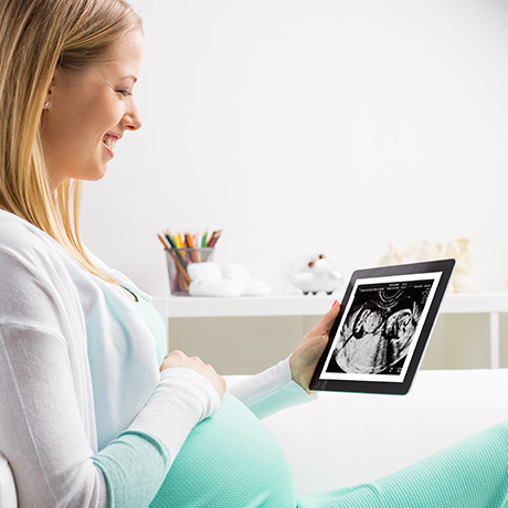 a pregnant woman sitting on a couch holding an electronic device